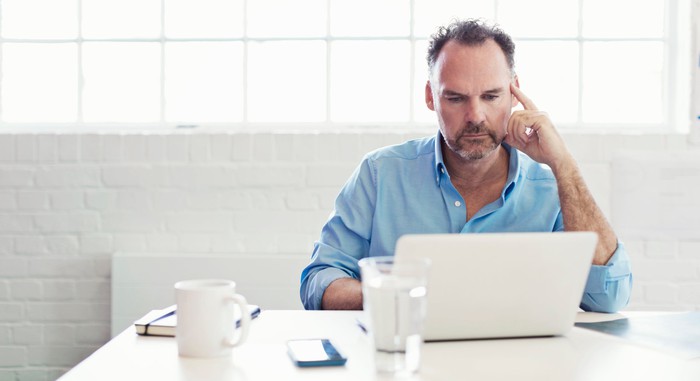 A middle-aged man of serious expression on a laptop