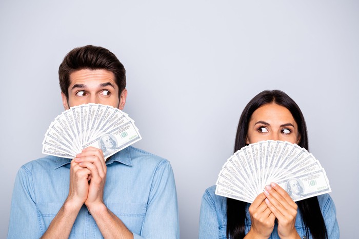 A man and a woman hold fans of $ 100 bills. 