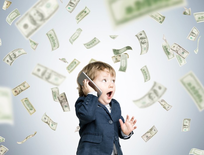 A toddler on a smartphone under a rain of money. 