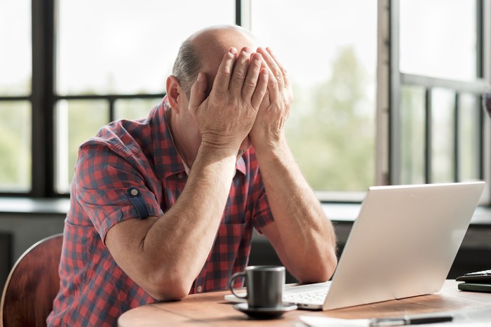 The man behind the laptop covers his face