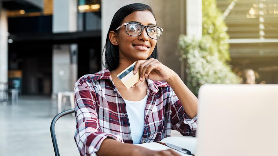 Cut-out shot of a young female student using a laptop and credit card outside on campus.