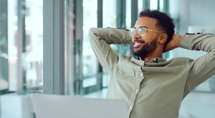 A smiling person on a laptop looks out the window