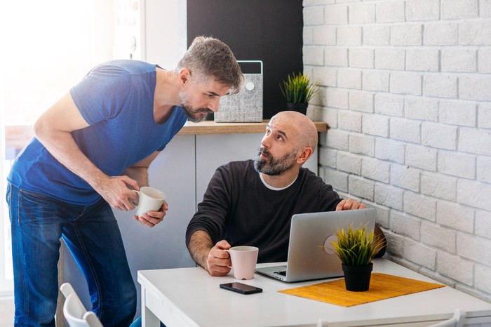 Two people are talking about something while one is looking at a laptop screen